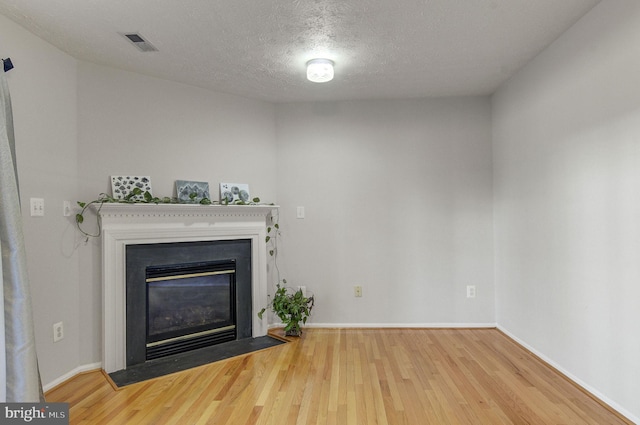 unfurnished living room with baseboards, visible vents, a fireplace with flush hearth, wood finished floors, and a textured ceiling