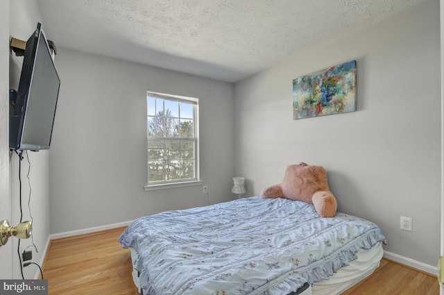 bedroom featuring a textured ceiling, wood finished floors, and baseboards