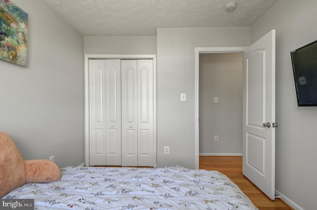 bedroom featuring a closet, baseboards, a textured ceiling, and light wood finished floors