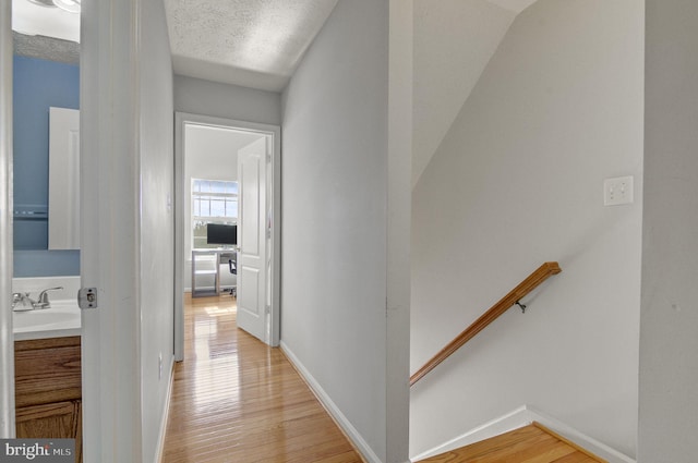 corridor with light wood finished floors, a textured ceiling, a sink, and an upstairs landing