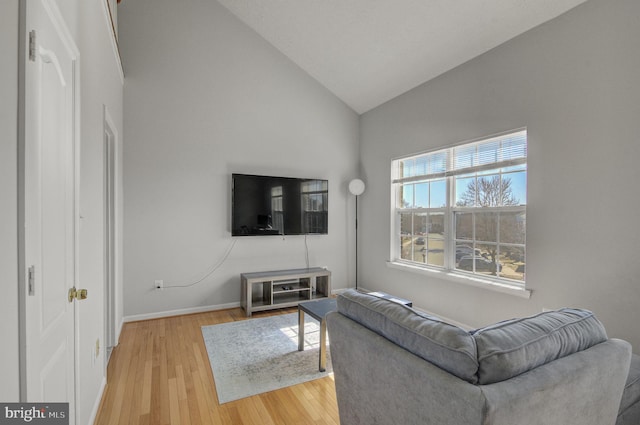 living room featuring lofted ceiling, light wood finished floors, and baseboards