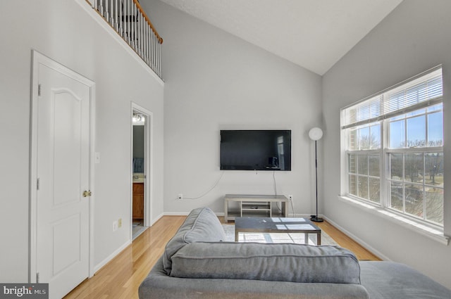 living room featuring high vaulted ceiling, baseboards, and wood finished floors