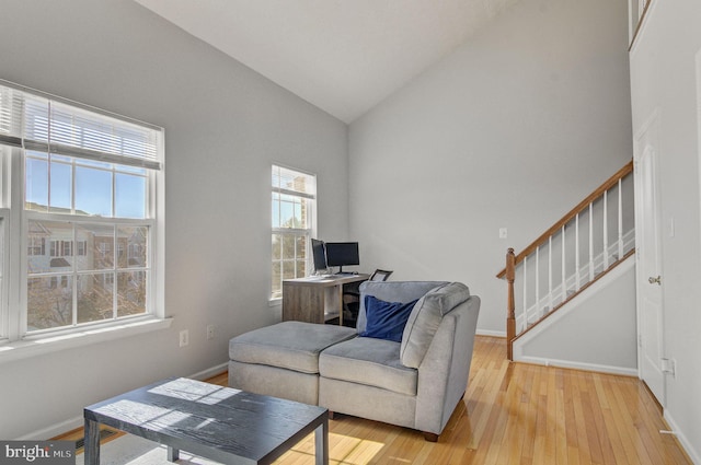 living area with lofted ceiling, light wood-style flooring, stairs, and baseboards