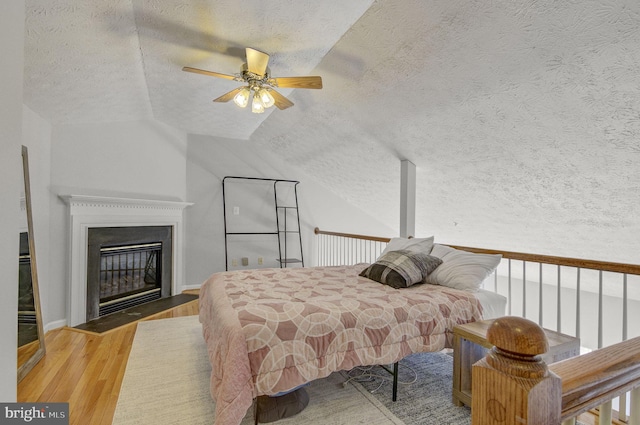 bedroom featuring vaulted ceiling, a fireplace with flush hearth, a textured ceiling, and wood finished floors