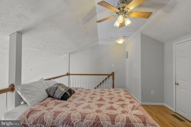 bedroom with visible vents, ceiling fan, vaulted ceiling, a textured ceiling, and wood finished floors