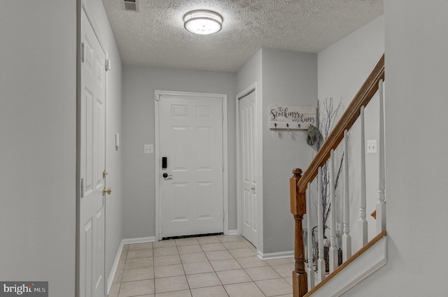 foyer featuring light tile patterned floors, a textured ceiling, stairs, and baseboards