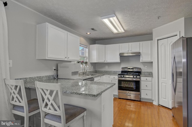 kitchen with under cabinet range hood, stainless steel appliances, a peninsula, a sink, and white cabinetry