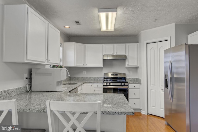 kitchen with appliances with stainless steel finishes, white cabinetry, under cabinet range hood, and a peninsula