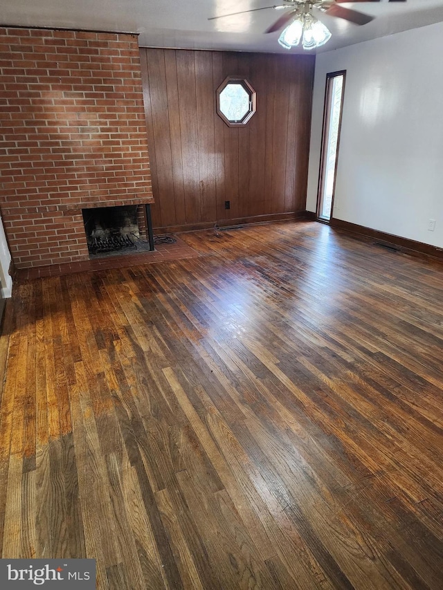 unfurnished living room featuring ceiling fan, a fireplace, baseboards, and wood finished floors