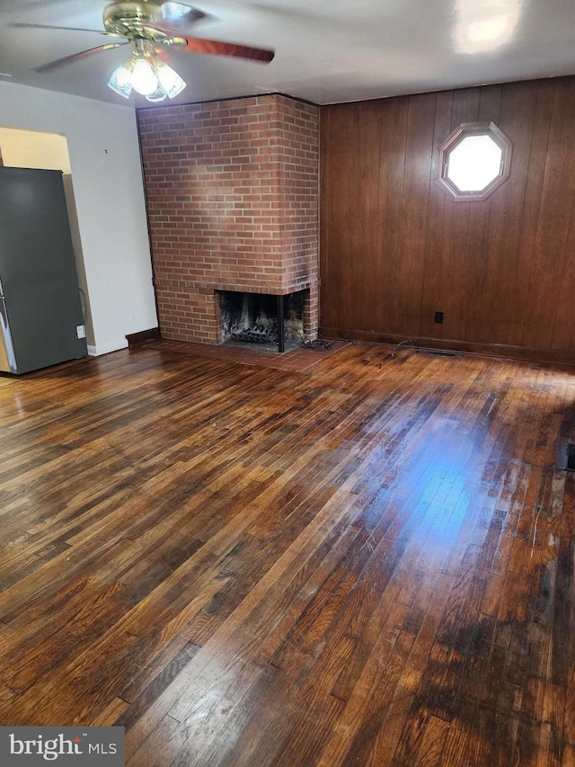 unfurnished living room with ceiling fan, wood walls, a fireplace, and wood-type flooring