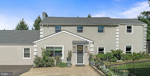 view of front of house with a shingled roof, a chimney, and stucco siding