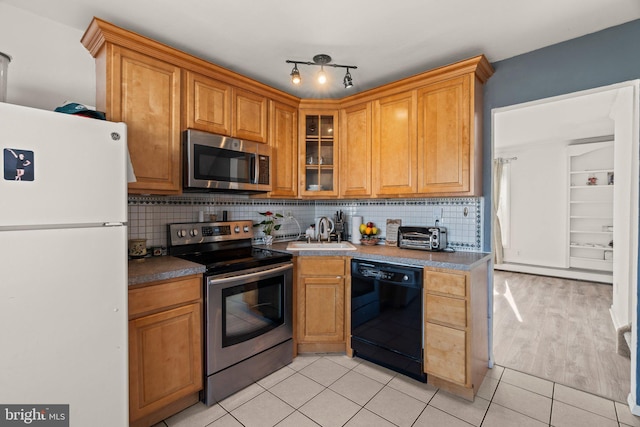 kitchen featuring light tile patterned floors, stainless steel appliances, backsplash, baseboard heating, and a sink