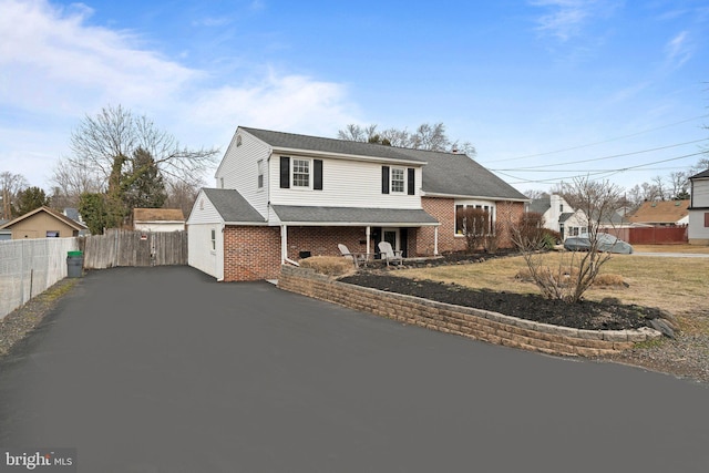 view of front of property with driveway, brick siding, and fence