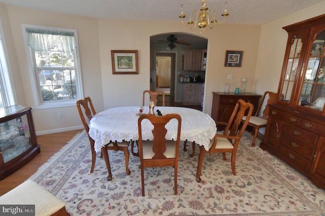 dining area with arched walkways, baseboards, light wood finished floors, and ceiling fan with notable chandelier