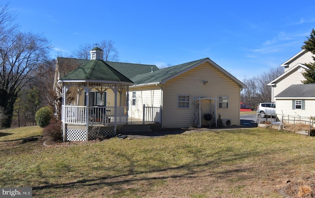 view of front facade featuring a front yard, roof with shingles, a chimney, and a gazebo