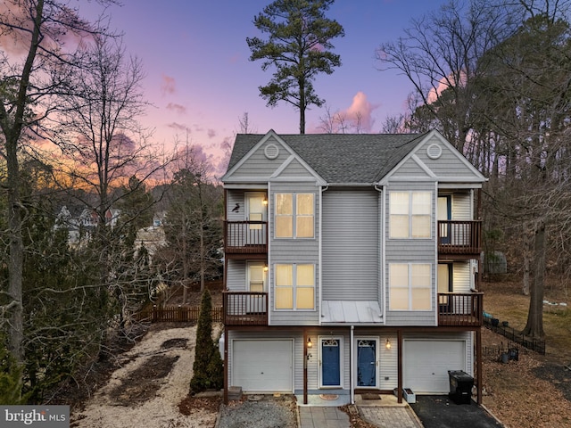 view of property with a garage, driveway, a shingled roof, and a balcony