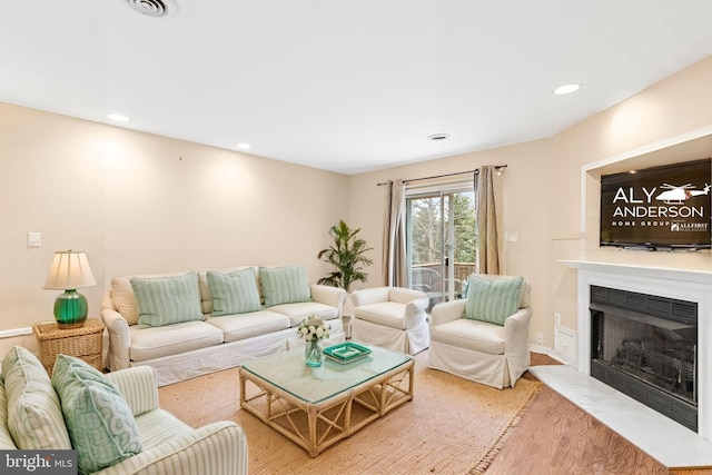 living room featuring recessed lighting, light wood-style flooring, visible vents, and a fireplace with flush hearth