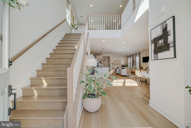 stairway with baseboards, wood finished floors, a towering ceiling, and recessed lighting