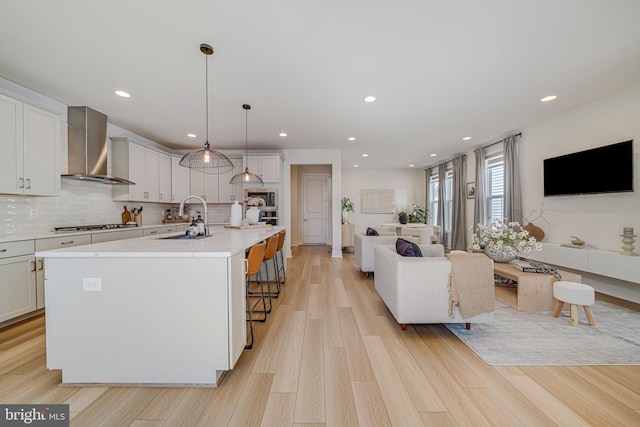 kitchen featuring light wood-style floors, wall chimney exhaust hood, open floor plan, and a sink