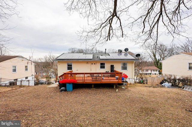 back of house with roof mounted solar panels, fence, and a wooden deck