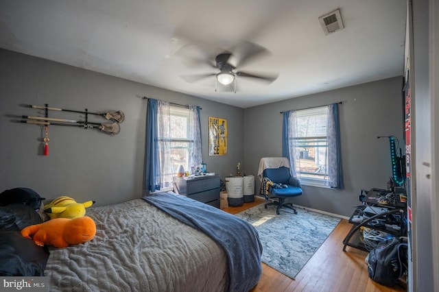 bedroom featuring ceiling fan, wood finished floors, visible vents, and baseboards