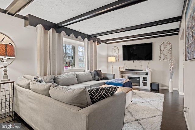 living area featuring dark wood-type flooring, a glass covered fireplace, beam ceiling, and baseboards