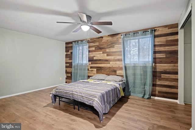 bedroom with a ceiling fan, wooden walls, baseboards, and wood finished floors