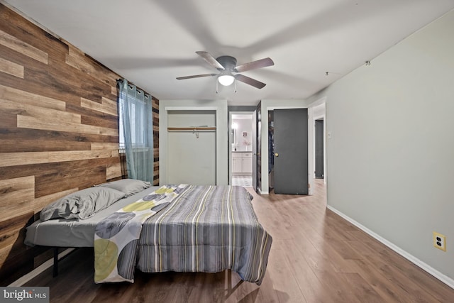 bedroom with ensuite bathroom, ceiling fan, wooden walls, wood finished floors, and baseboards