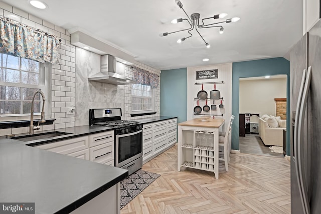 kitchen featuring tasteful backsplash, wall chimney exhaust hood, stainless steel appliances, white cabinetry, and a sink