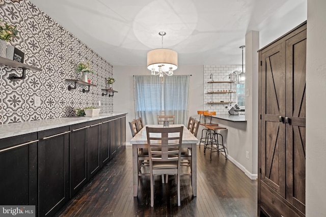 dining area featuring dark wood-style floors, an accent wall, a notable chandelier, and baseboards