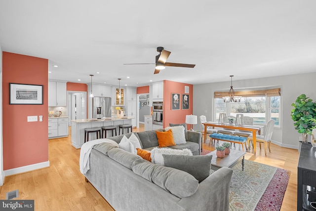 living room featuring visible vents, ceiling fan with notable chandelier, recessed lighting, light wood finished floors, and baseboards