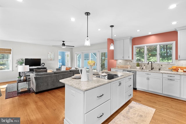 kitchen with light wood finished floors, a sink, dishwasher, black electric cooktop, and tasteful backsplash