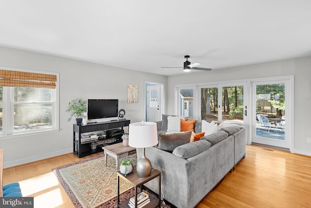 living area with baseboards, light wood-type flooring, a wealth of natural light, and ceiling fan