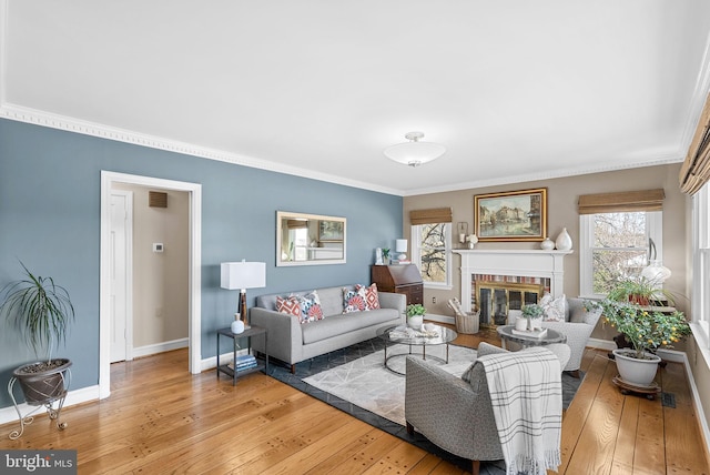 living area with baseboards, visible vents, a fireplace, light wood-style floors, and crown molding