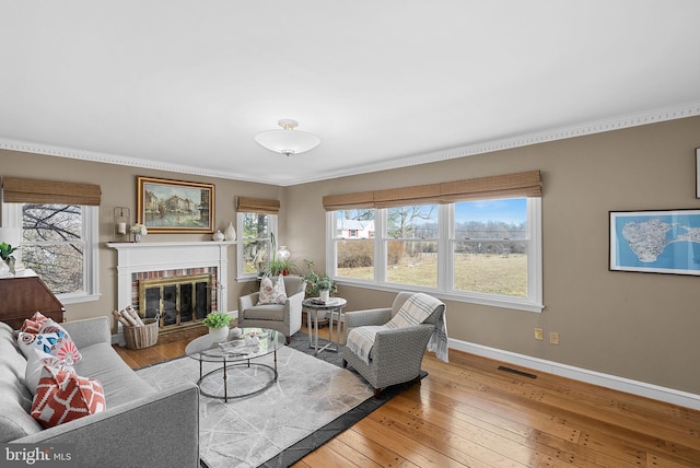 living area with visible vents, baseboards, hardwood / wood-style flooring, crown molding, and a brick fireplace