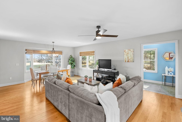 living room with ceiling fan with notable chandelier, baseboards, and light wood finished floors