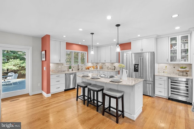 kitchen with light wood finished floors, wine cooler, appliances with stainless steel finishes, a kitchen breakfast bar, and a sink