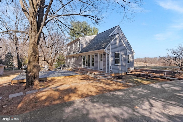 view of side of property featuring a wooden deck and roof with shingles