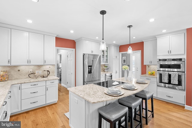 kitchen featuring light wood finished floors, a kitchen island, stainless steel appliances, white cabinets, and a kitchen breakfast bar