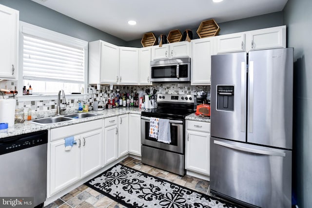 kitchen featuring backsplash, a sink, white cabinets, appliances with stainless steel finishes, and stone finish flooring