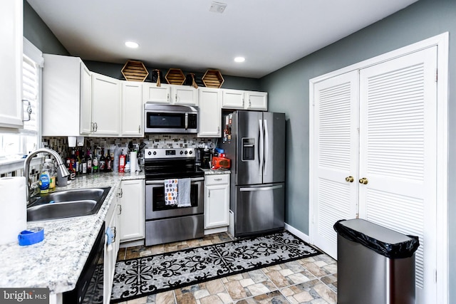 kitchen featuring light countertops, white cabinets, stone finish floor, stainless steel appliances, and a sink
