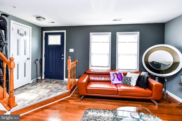 living room featuring baseboards, visible vents, wood finished floors, and stairs