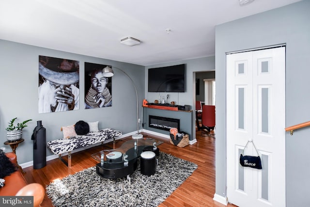 living room with a glass covered fireplace, baseboards, and wood finished floors