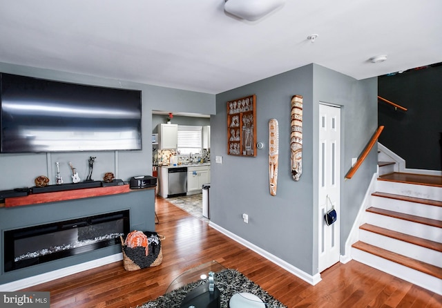 living room with stairs, wood finished floors, baseboards, and a glass covered fireplace