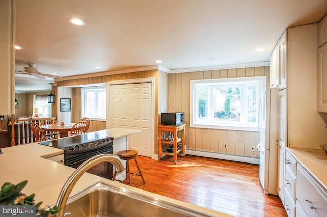 kitchen featuring freestanding refrigerator, black / electric stove, light countertops, light wood-style floors, and a baseboard heating unit