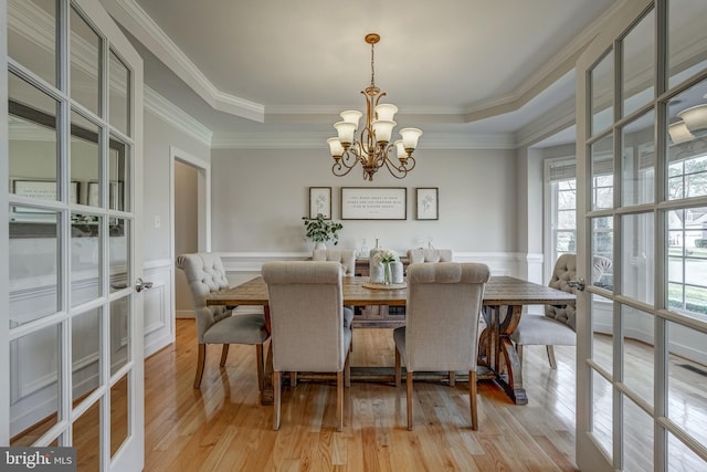 dining space with light wood-type flooring, a wainscoted wall, a tray ceiling, and a notable chandelier