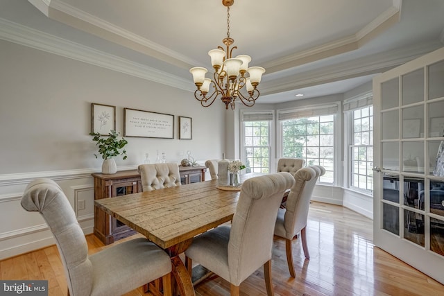 dining area with crown molding, a raised ceiling, a decorative wall, wainscoting, and light wood-type flooring