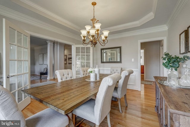 dining area featuring decorative columns, wainscoting, ornamental molding, light wood-style floors, and a chandelier