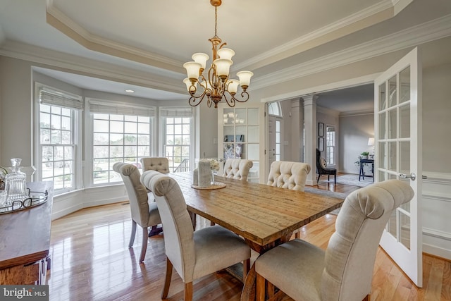 dining space with light wood-type flooring, ornate columns, a tray ceiling, and french doors