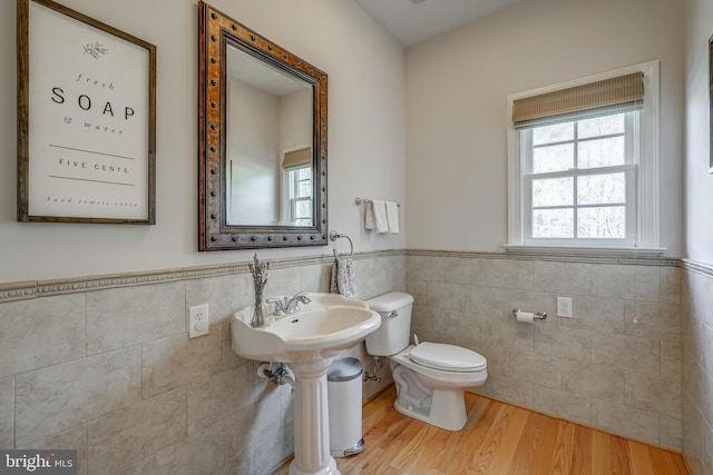 bathroom with toilet, a wainscoted wall, tile walls, and wood finished floors